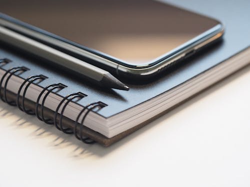 Foto De Primer Plano Del Teléfono Inteligente Negro Cerca De Lápiz Negro Y Gris Sobre Negro Cuaderno De Espiral