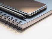 特写镜头聚焦在桌上的螺旋笔记本、智能手机和铅笔，突显了现代工作空间的必备物品