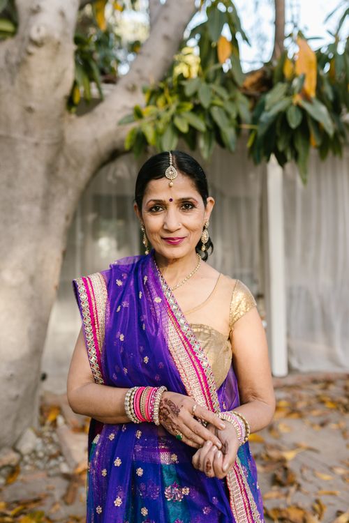 Free Graceful Indian woman in a vibrant saree and jewelry, standing outdoors with trees. Stock Photo