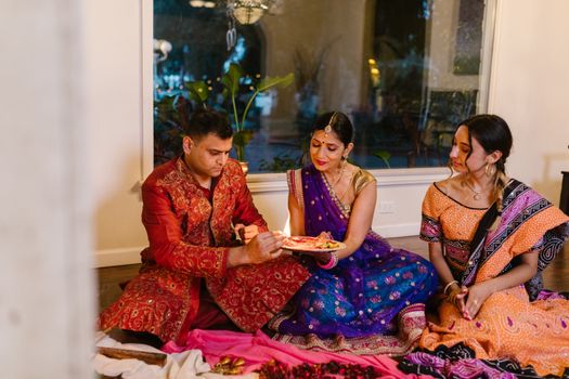 A family partakes in a traditional Indian ritual indoors, showcasing cultural attire and customs.