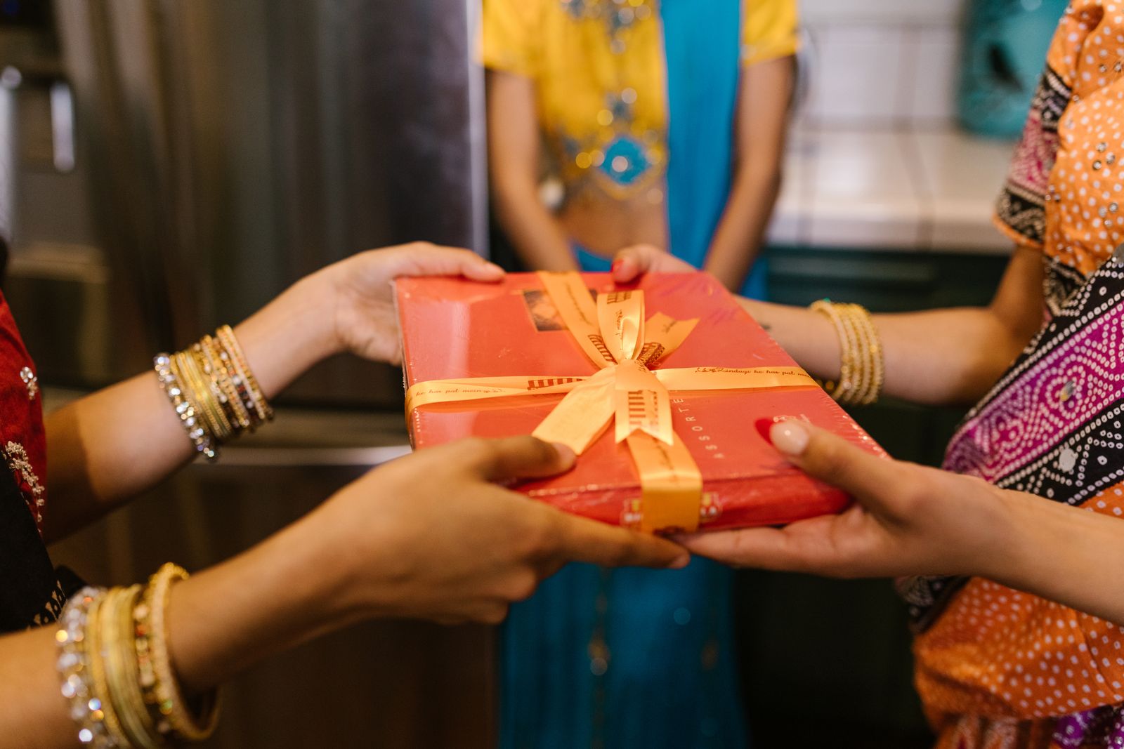 Close-up of women exchanging a gift during a colorful, cultural celebration.