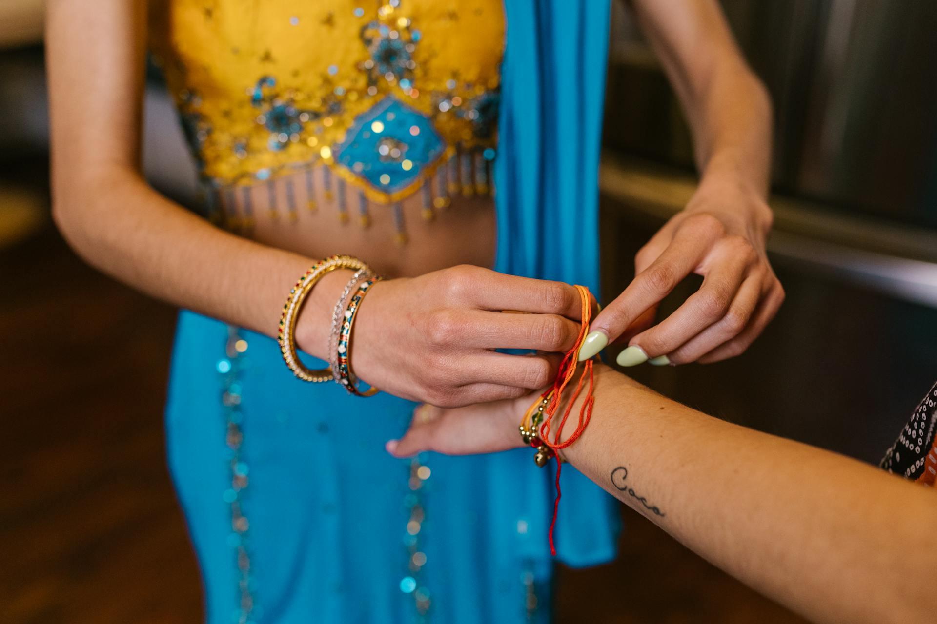 Close-up of a woman tying a decorative bracelet during a traditional Raksha Bandhan ceremony.