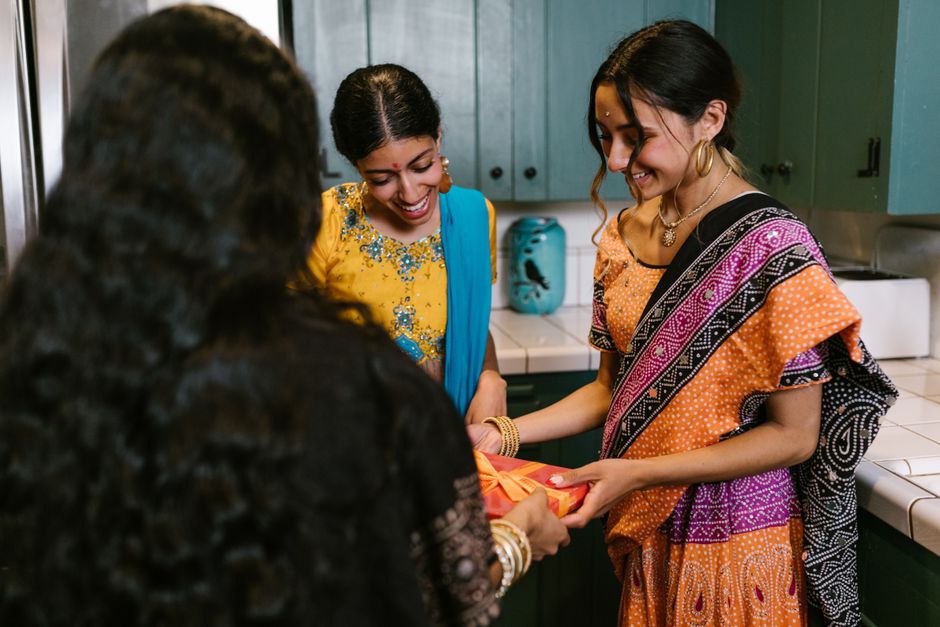 Three women in traditional attire sharing gifts during a Diwali celebration indoors.