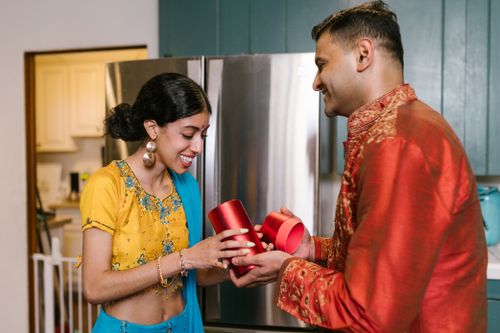 Free A man and woman exchange Diwali gifts in a festive kitchen setting, wearing traditional clothing. Stock Photo
