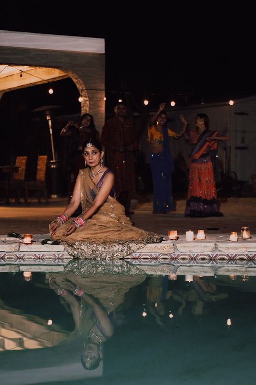Free An Indian woman in a sari sits by a poolside with candles around, capturing a cultural evening scene. Stock Photo