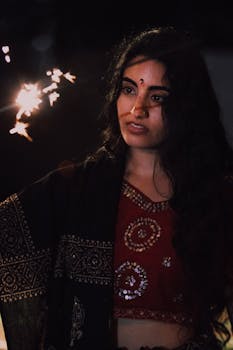 A woman in traditional Indian attire holding a glowing sparkler at night, creating a festive atmosphere.