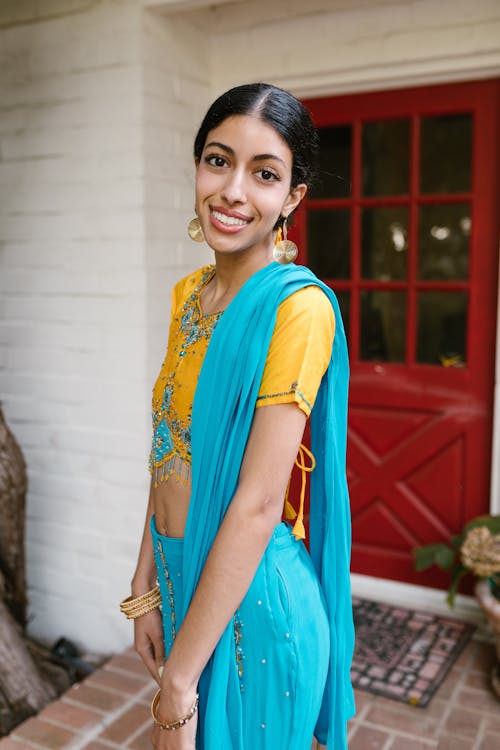 Woman in Blue and Yellow Sari Standing Near Red Wooden Door