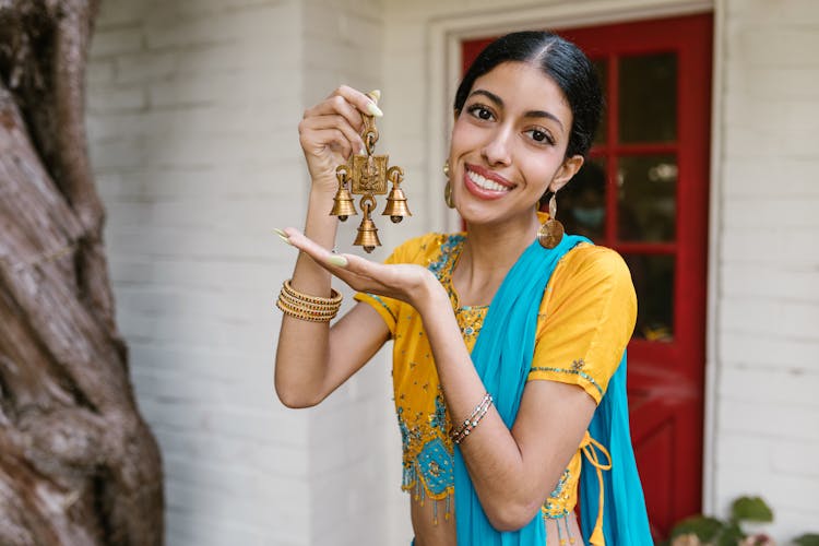 Woman In Yellow And Blue Sari Holding A Gold Ornament