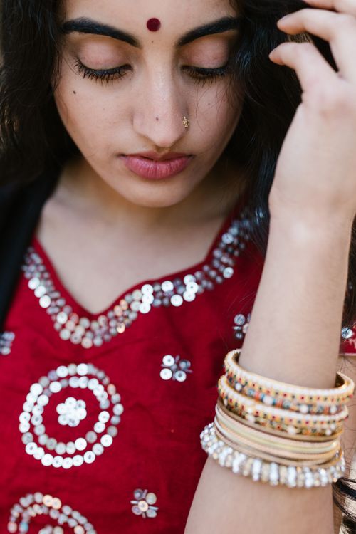 Free Close-up of a South Asian woman in a red sequined top with bracelets, looking serene. Stock Photo