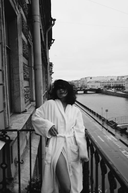 Free Black and white confident female with short dark hair in bathrobe standing on balcony above road near canal Stock Photo