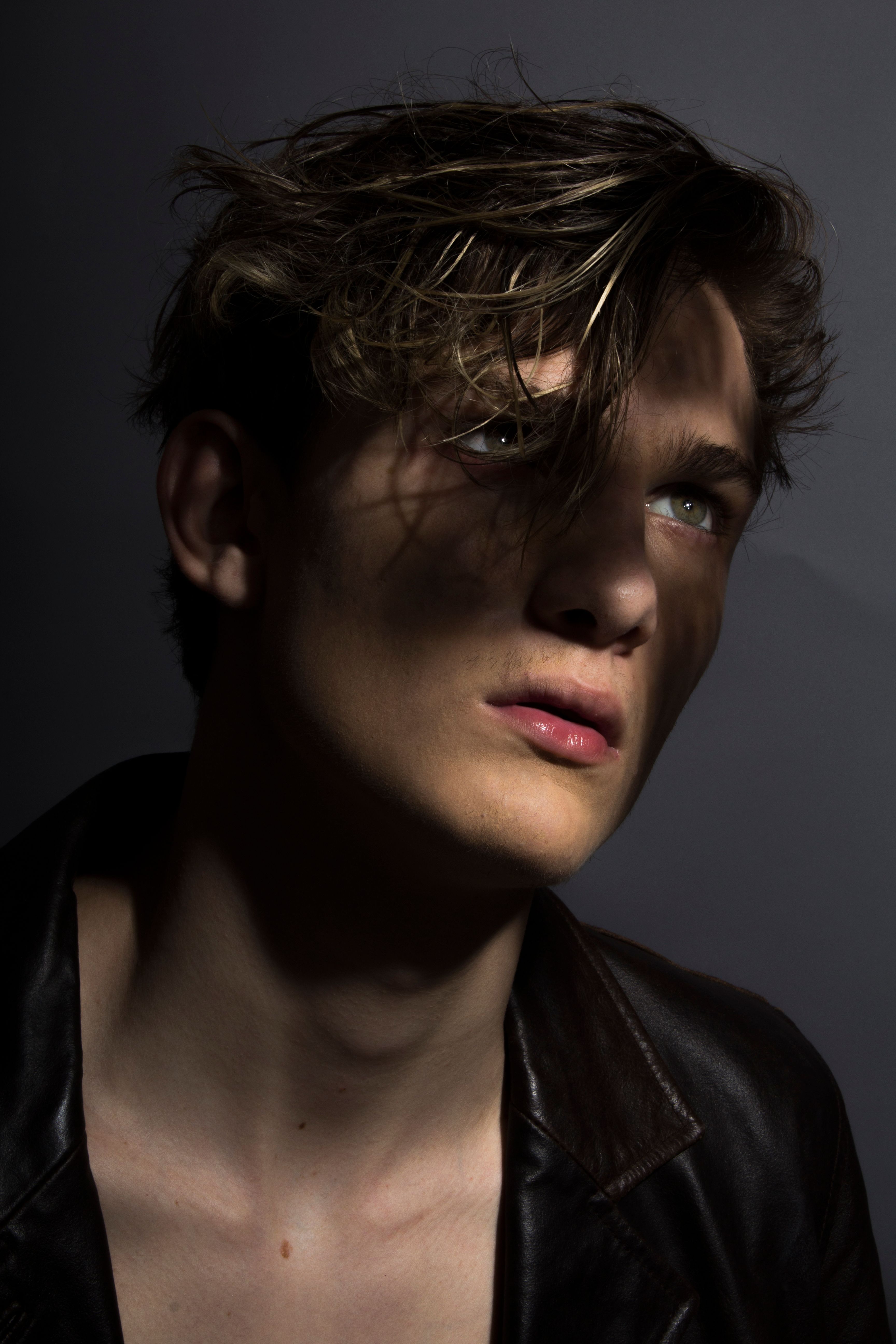 Artistic portrait of a young man with dramatic lighting and shadows, creating a moody effect.