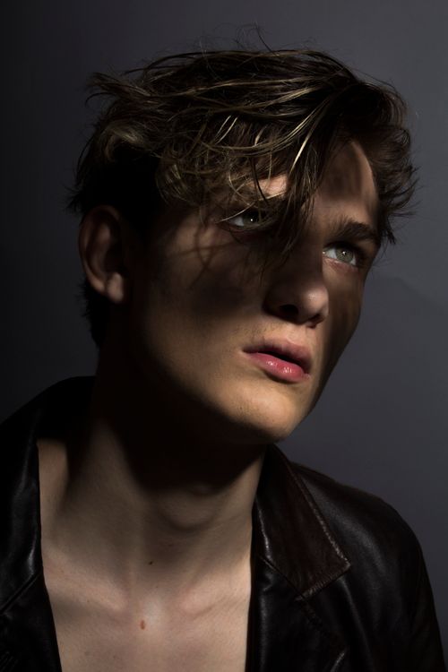 Free Artistic portrait of a young man with dramatic lighting and shadows, creating a moody effect. Stock Photo