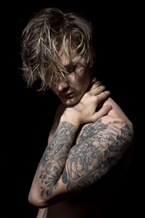 Free Expressive portrait of a tattooed shirtless man with a moody shadow play on his face, highlighting intricate tattoos. Stock Photo