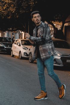 Young man in fashionable attire walking on city street with cars parked, creative urban lifestyle.
