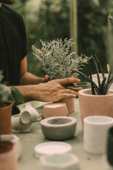 Close-up of hands arranging potted plants on a table with minimalist decor in a serene garden setting.