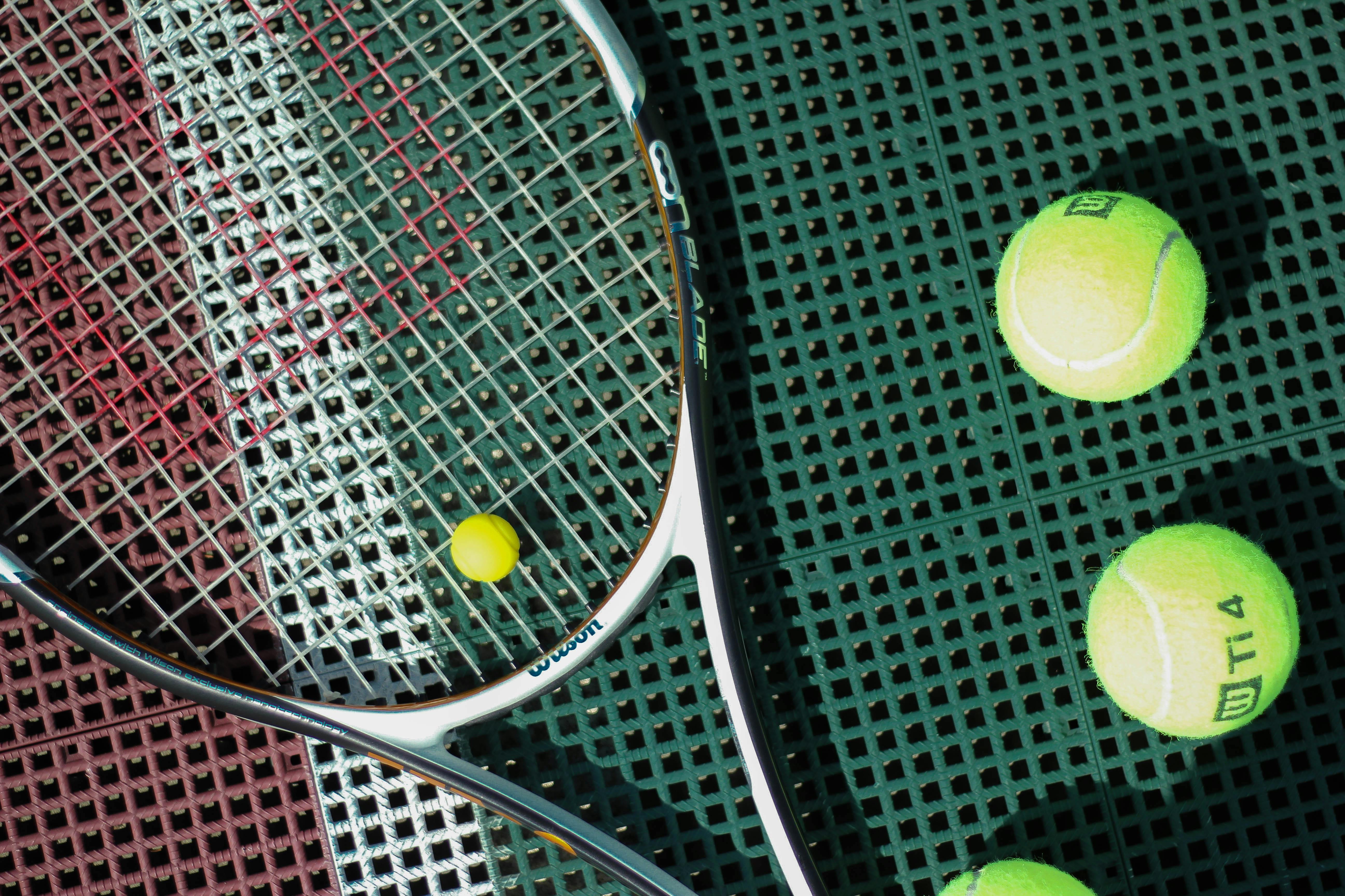 Top view of a tennis racket and balls on an outdoor court surface.