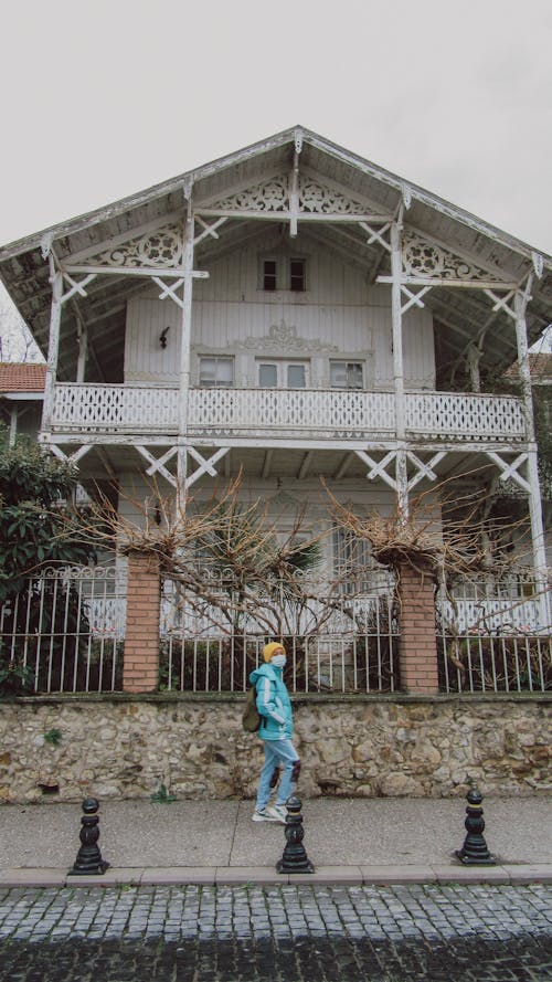A Person Wearing Face Mask Passing by a White Wooden House