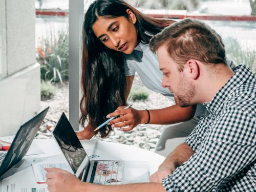 Free Two colleagues in a bright office sharing ideas and working on laptops, promoting teamwork. Stock Photo