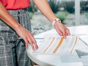 Person in Red Shirt and Gray and White Plaid Pants Holding White Book
