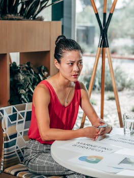 Woman in red top attentively discussing marketing strategy in modern office setting.
