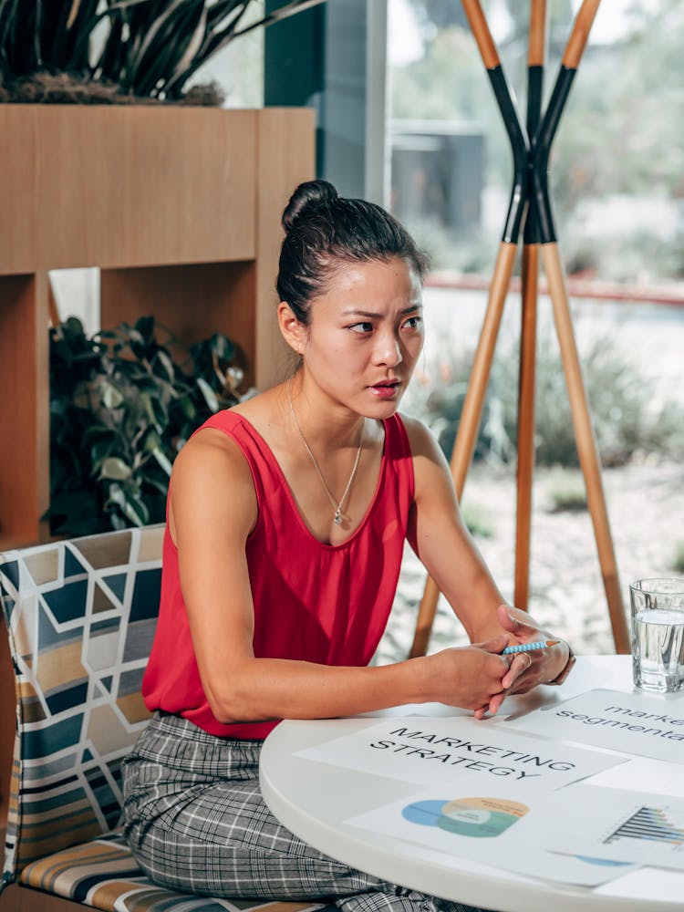 Serious Asian Marketer Speaking At Desk With Papers In Office