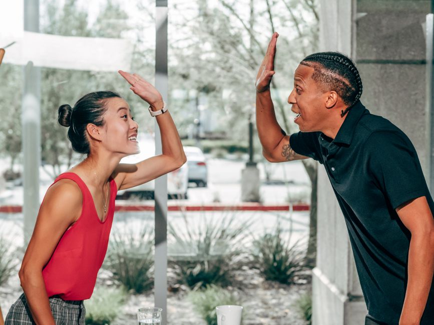 Uma troca alegre entre colegas compartilhando um high-five dentro de um escritório moderno.