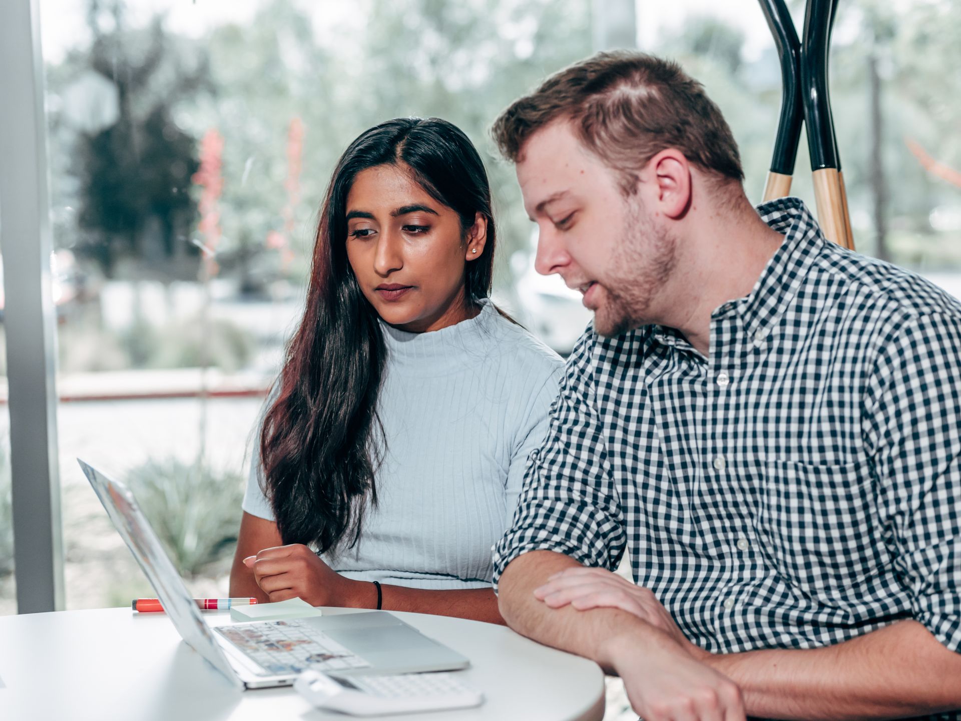 A man and woman discussing work on a laptop during a team meeting indoors.