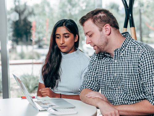Free A man and woman discussing work on a laptop during a team meeting indoors. Stock Photo