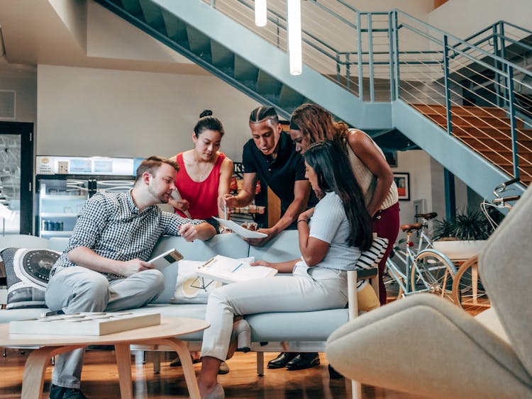 Group Of People Sitting On White Couch In The Office Lobby While Looking At A Document