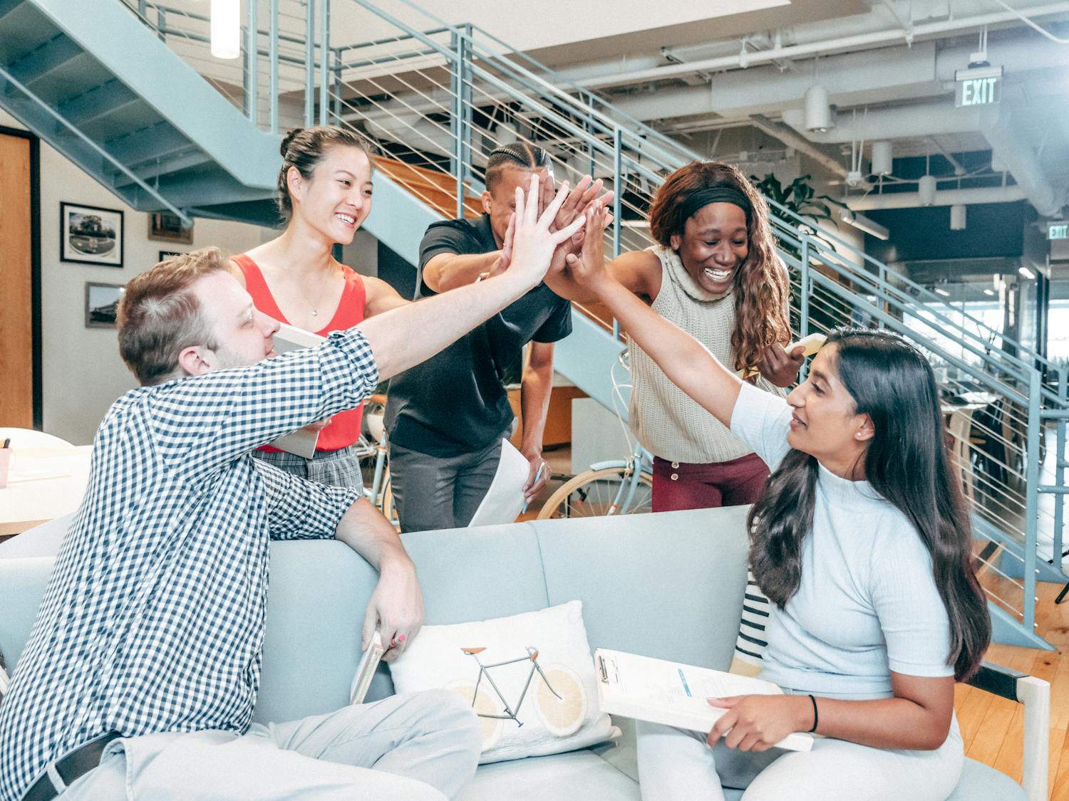 A diverse team celebrates success with a high-five in a modern office setting.