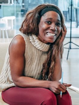 Smiling woman sitting comfortably with a notebook and pencil indoors in a casual environment.