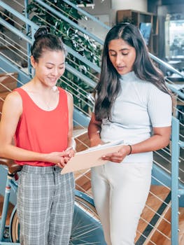 Two women discussing work on a clipboard in a modern office space, promoting collaboration and teamwork.