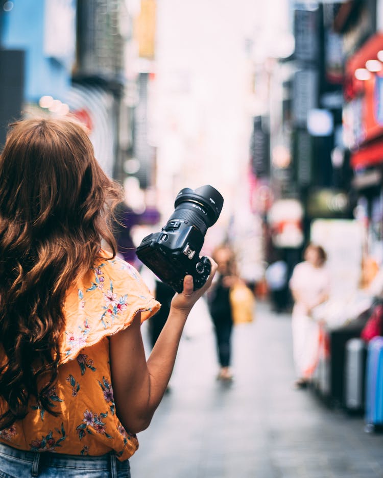 Woman In Floral Blouse Holding Black Dslr Camera