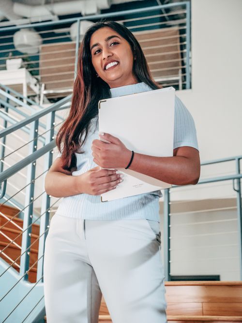 Free Confident woman smiles while holding documents on a modern indoor staircase. Stock Photo