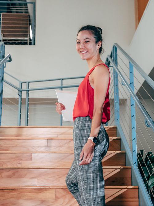 Free Smiling woman in a red top climbing stairs, representing professional confidence. Stock Photo