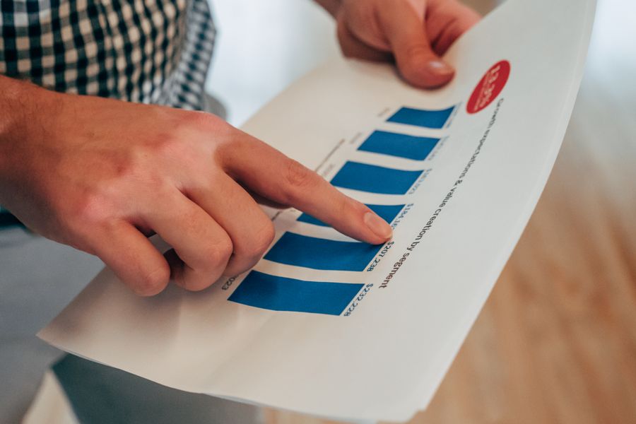 Close-up of hands pointing at a bar chart on paper, analyzing financial stats and report.