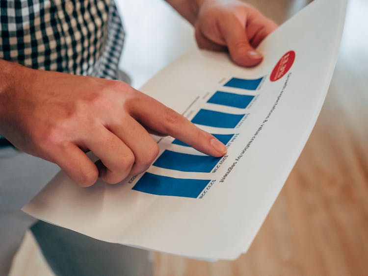 A Person Holding A Report With Chart Pointing On A  Number