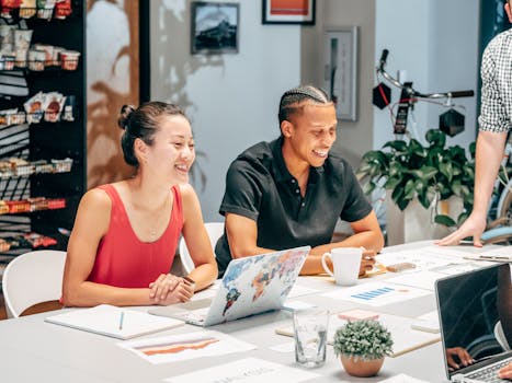 Smiling colleagues brainstorming at work around a table with laptops and documents.