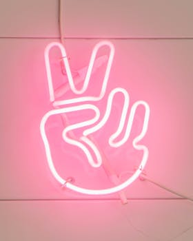 Bright pink neon peace sign glowing against a wall.