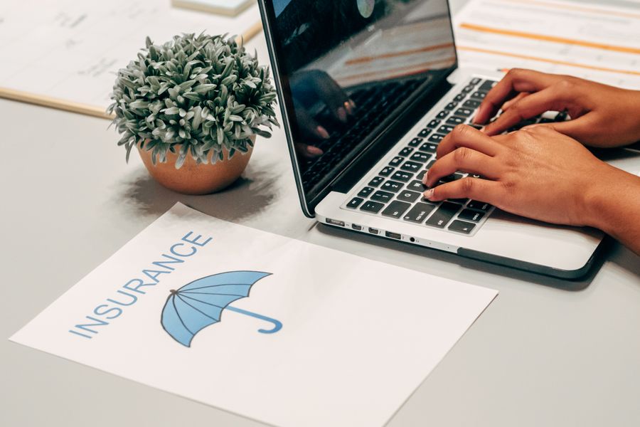 Hands typing on a laptop beside an insurance document on a home desk