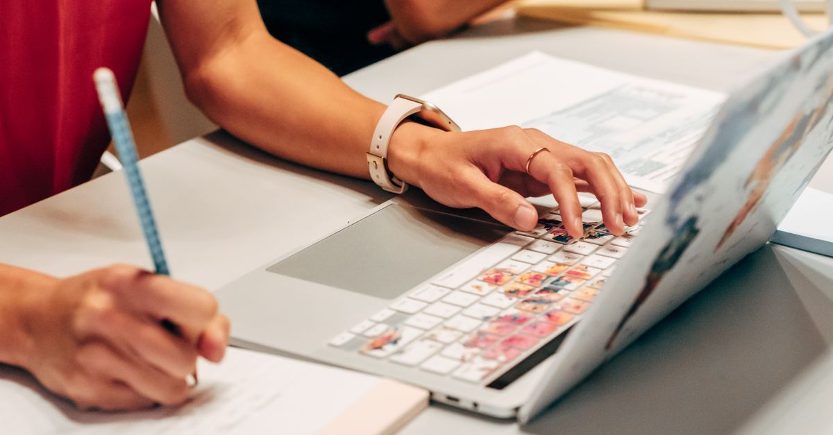 close-up of hands writing an essay on a desk with laptop