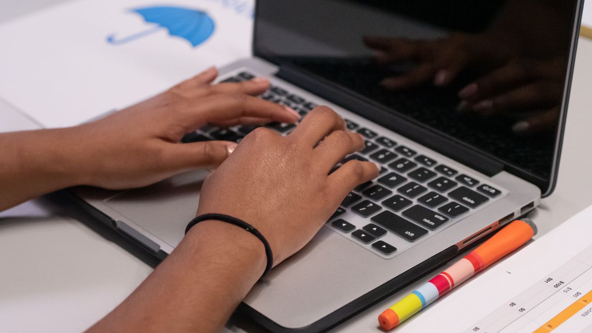 A person works on a laptop with colorful markers and a printed chart nearby.
