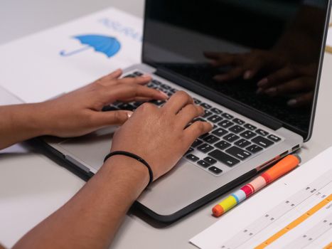 A person works on a laptop with colorful markers and a printed chart nearby.