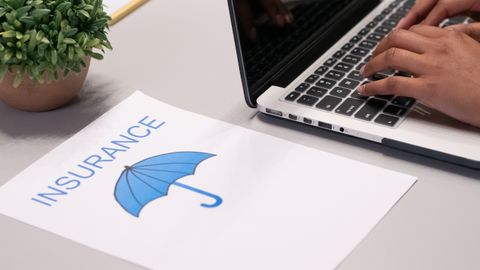 Close-up of hands typing on laptop with an insurance document visible on the desk.