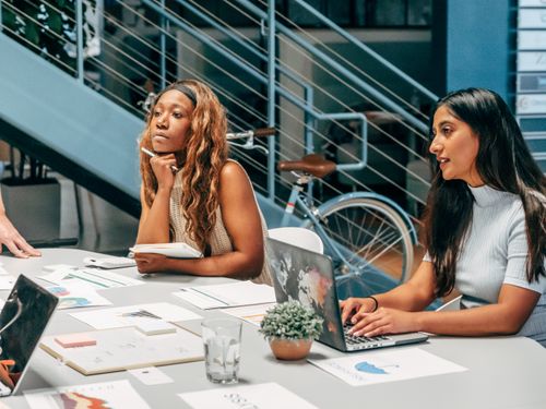 Free Diverse women engaging in a collaborative meeting at an office desk, focused on planning and innovation. Stock Photo