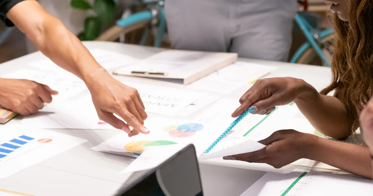 Hands pointing at printed charts and graphs on a table while colleagues look on, representing SEC AI governance examination