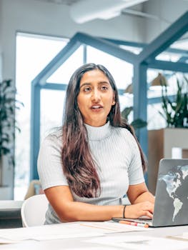 Confident professional woman working at a laptop in a bright modern office.
