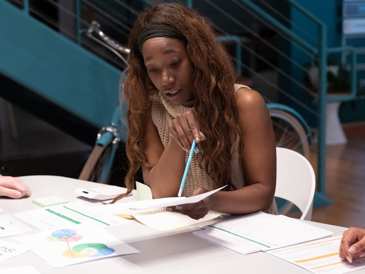 A Woman Sitting At A Desk Pointing A Pen On A Paper On Her Hand