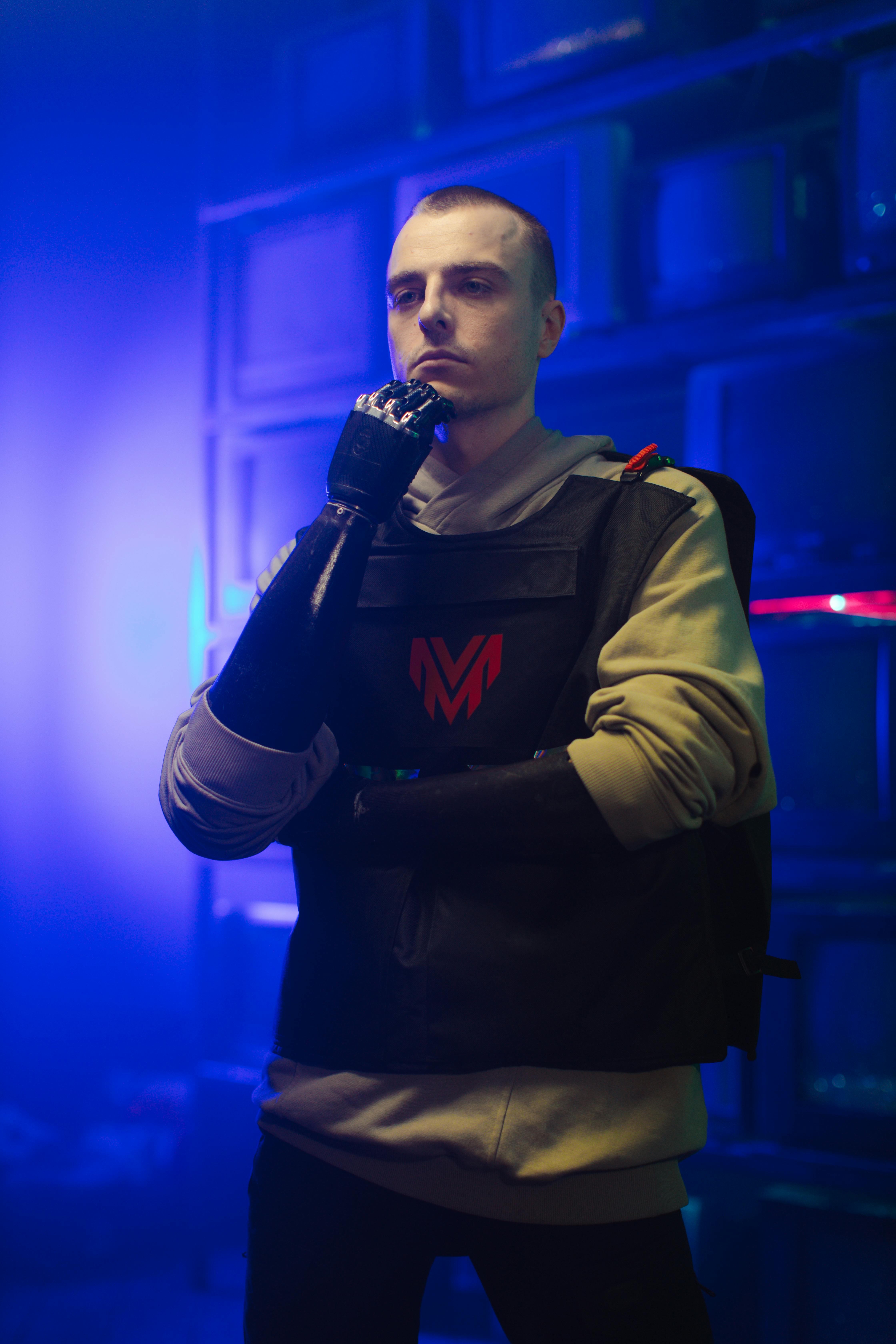 A fashionable man confidently poses with a prosthetic hand in a vibrant, futuristic environment.