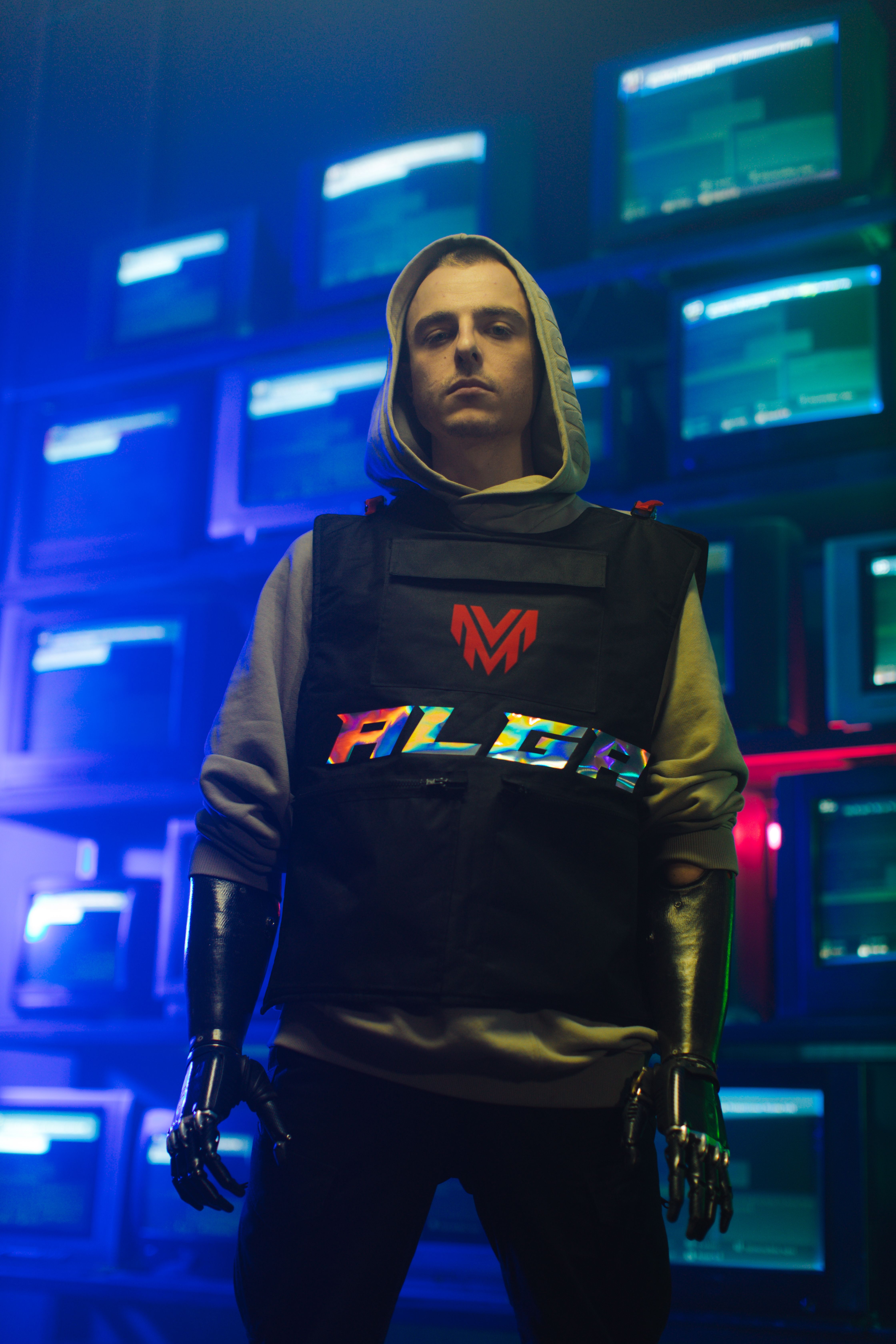 Portrait of a stylish man with prosthetic hands in a neon-lit room full of screens.